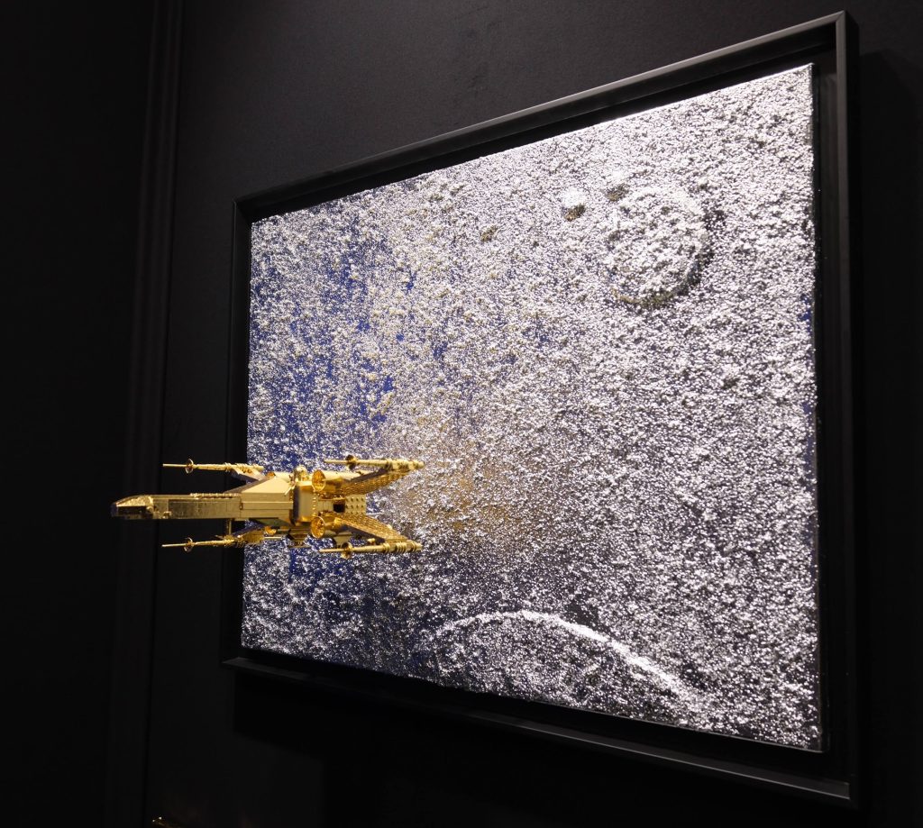 Seb Machten contemporary artwork with gold starfighter built from construction bricks emerging from lunar textured surface