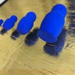Seb Machten contemporary artwork with blue matryoshka figures arranged in progression on textured gold leaf surface background
