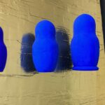 Seb Machten contemporary artwork with blue matryoshka figures arranged in progression on textured gold leaf surface background