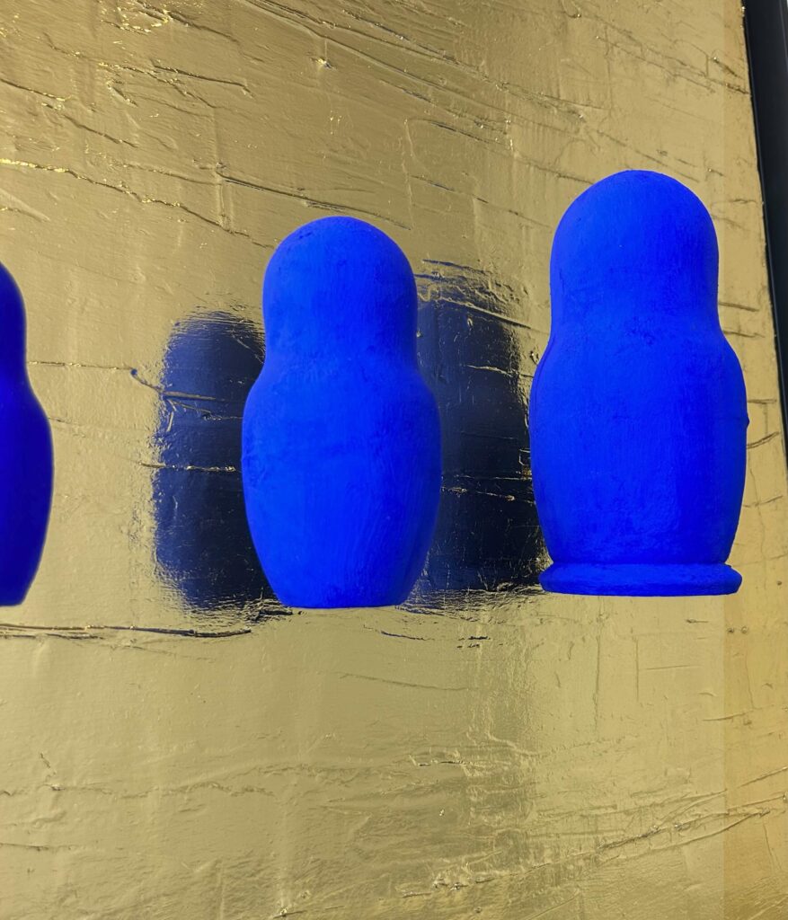 Seb Machten contemporary artwork with blue matryoshka figures arranged in progression on textured gold leaf surface background