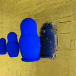 Seb Machten contemporary artwork with blue matryoshka figures arranged in progression on textured gold leaf surface background