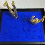 Seb Machten Contemporary pop art sculpture of two gold flying figures emerging and diving into textured gold surface, exploring illusion of escape and inner tension