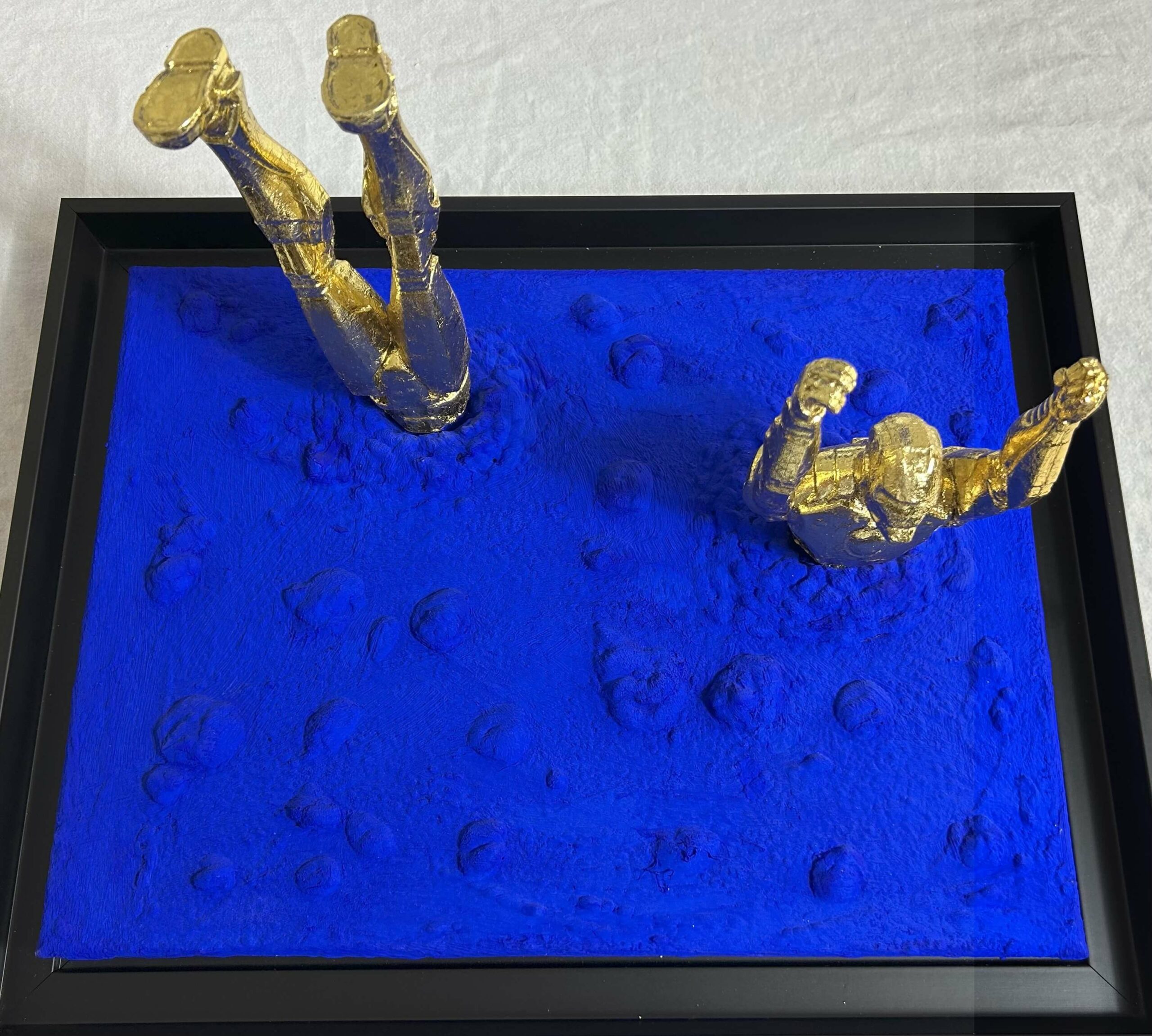 Seb Machten Contemporary pop art sculpture of two gold flying figures emerging and diving into textured gold surface, exploring illusion of escape and inner tension