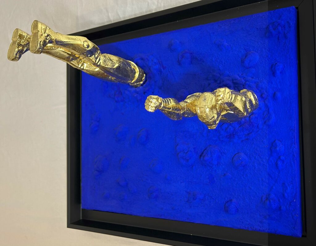 Seb Machten Contemporary pop art sculpture of two gold flying figures emerging and diving into textured gold surface, exploring illusion of escape and inner tension