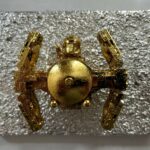 Seb Machten contemporary artwork with gold starfighter built from construction bricks projecting from textured silver surface