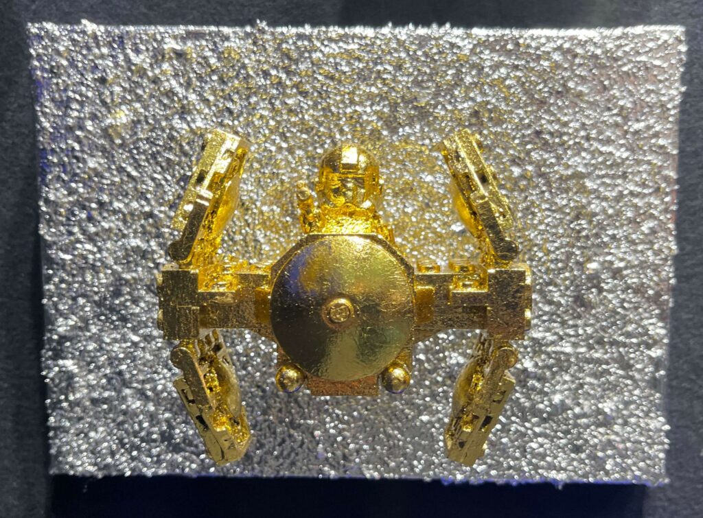 Seb Machten contemporary artwork with gold starfighter built from construction bricks projecting from textured silver surface