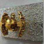 Seb Machten contemporary artwork with gold starfighter built from construction bricks projecting from textured silver surface