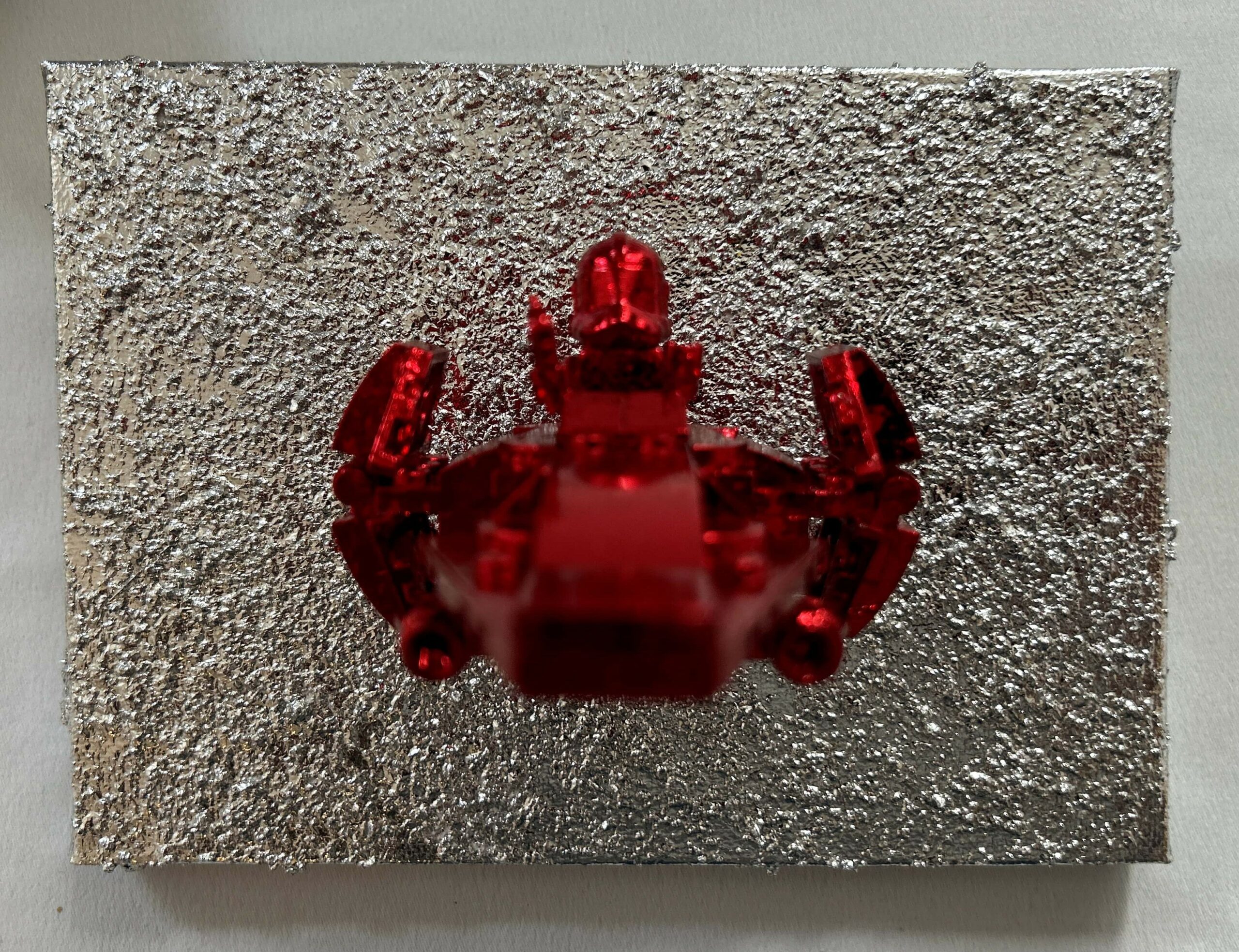 Seb Machten contemporary artwork with red starfighter built from construction bricks projecting from textured silver surface