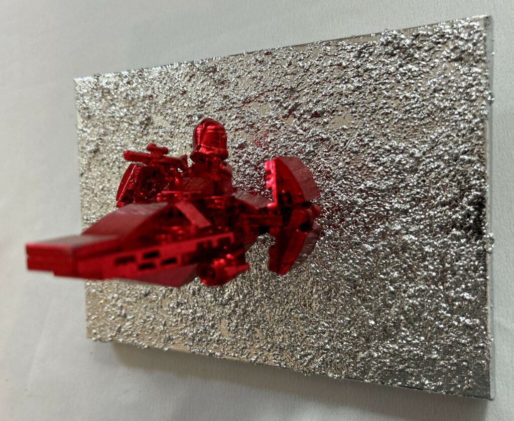 Seb Machten contemporary artwork with red starfighter built from construction bricks projecting from textured silver surface