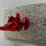 Seb Machten contemporary artwork with red starfighter built from construction bricks projecting from textured silver surface