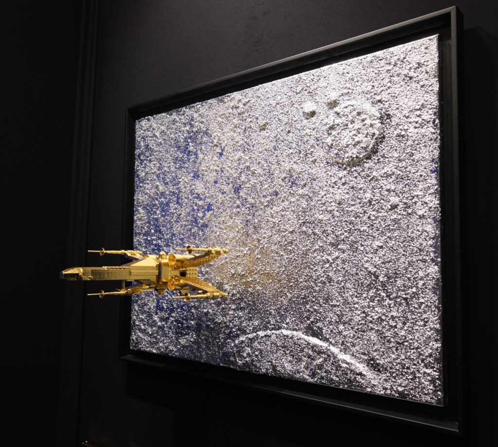 Seb Machten contemporary artwork with gold starfighter built from construction bricks emerging from lunar textured surface
