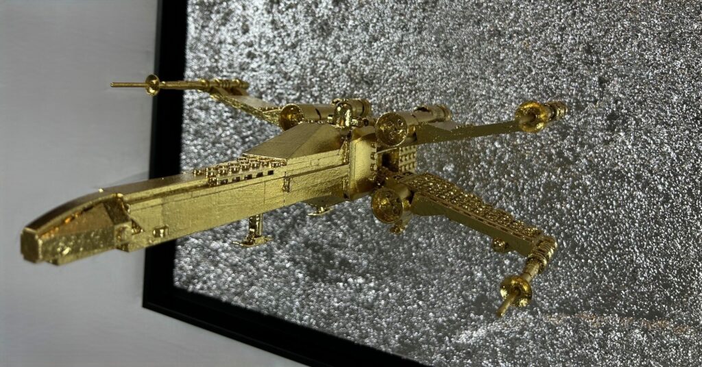 Seb Machten contemporary artwork with gold starfighter built from construction bricks emerging from lunar textured surface