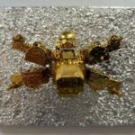 Seb Machten contemporary artwork with gold starfighter built from construction bricks projecting from textured silver surface