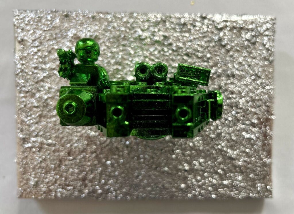 Seb Machten contemporary artwork with green starfighter built from construction bricks projecting from textured silver surface