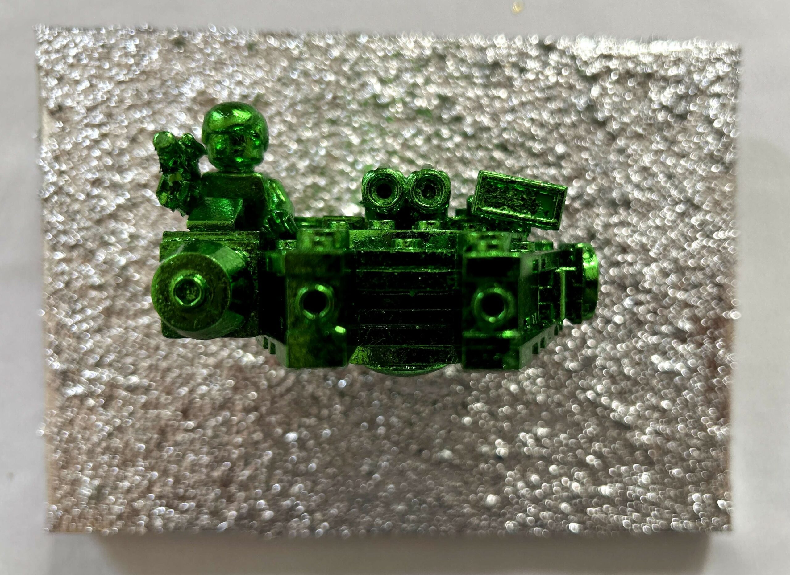 Seb Machten contemporary artwork with green starfighter built from construction bricks projecting from textured silver surface