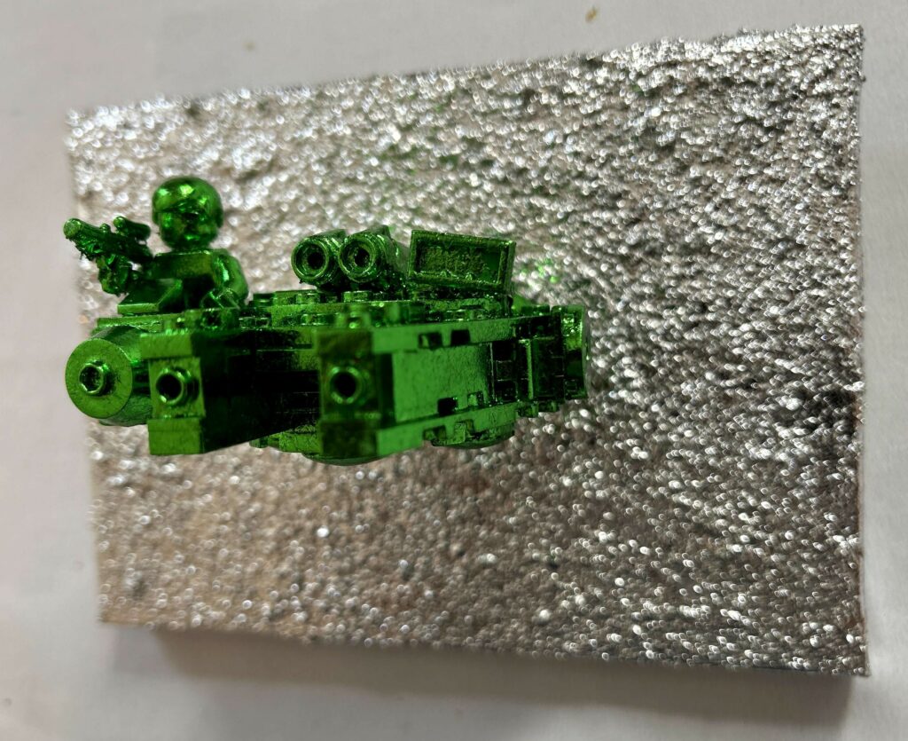 Seb Machten contemporary artwork with green starfighter built from construction bricks projecting from textured silver surface