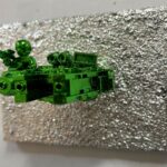 Seb Machten contemporary artwork with green starfighter built from construction bricks projecting from textured silver surface