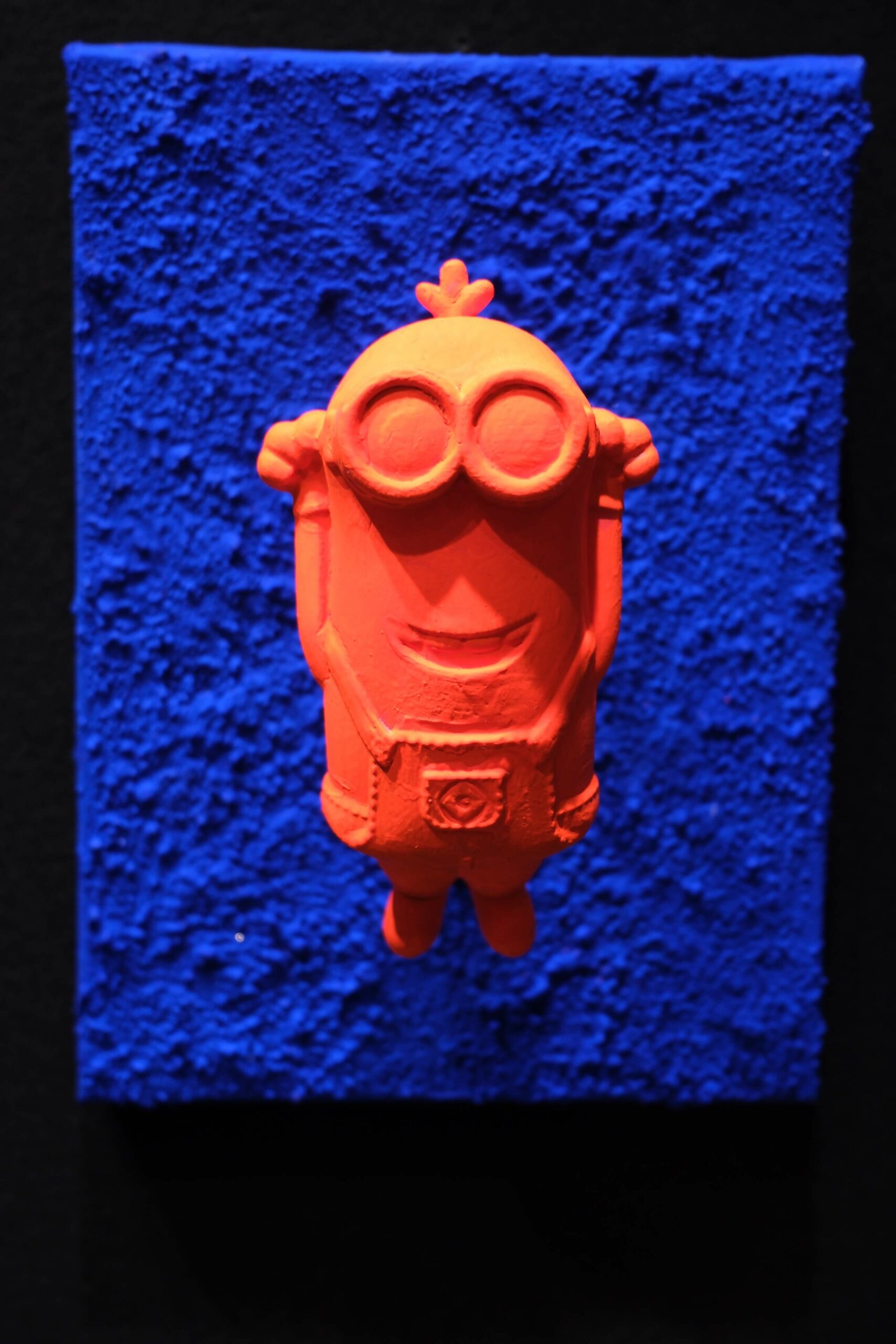 Seb Machten Contemporary pop art sculpture of an orange joyful character raising arms on deep blue textured background, symbolizing celebration, boldness and limitless possibility